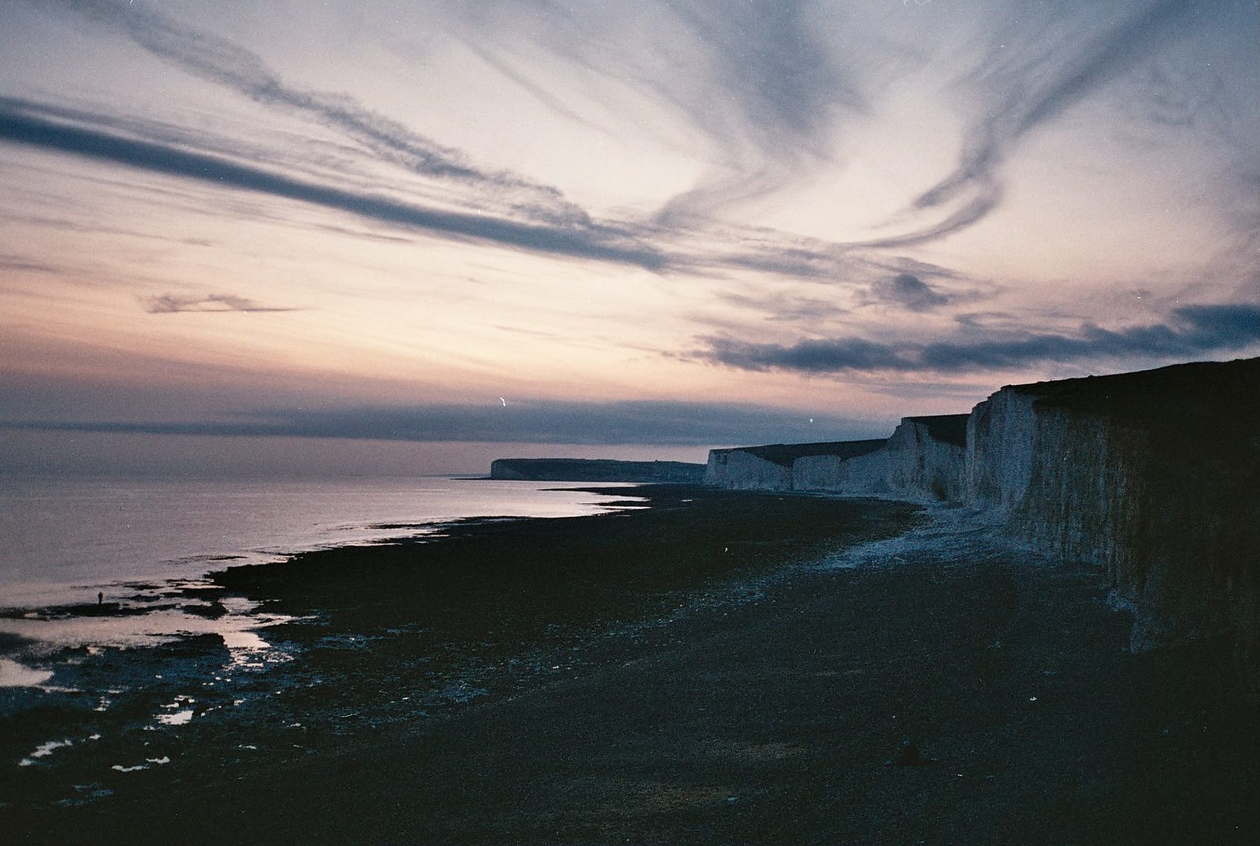 White chalk cliffs and a long shingle shore under a streaked pink and grey evening sky