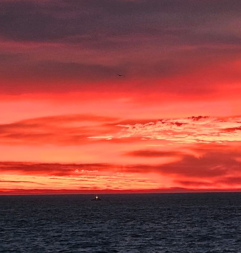 Red sky over a dark sea with a small boat on the horizon